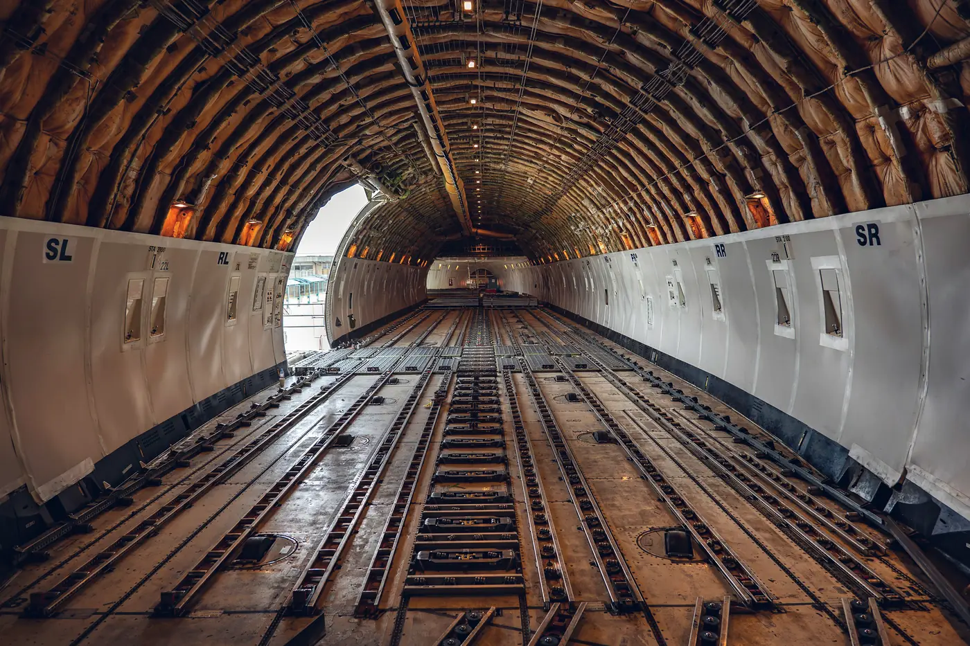 Empty main deck of a cargo aircraft, with roller tracks on the floor and daylight coming through the open side cargo door